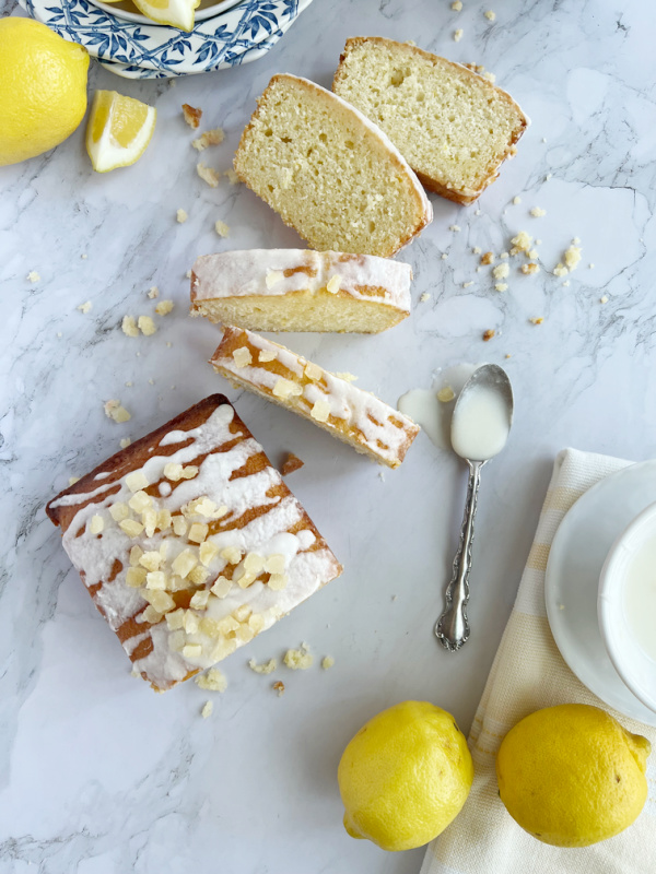 Sliced lemon pound cake with two lemons and a spoon of lemon glaze.