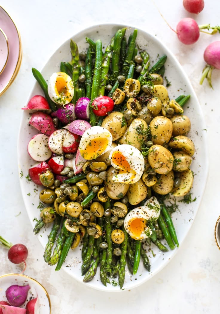 spring nicoise salad with potatoes, asparagus, radishes, hard boiled eggs on an white oval platter. 