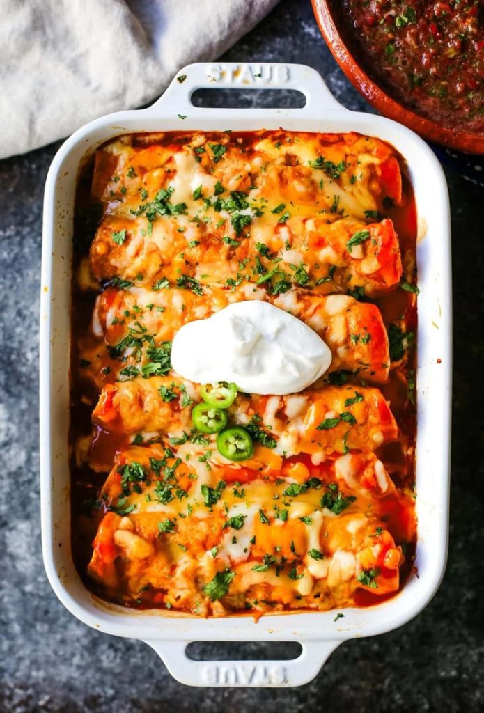 Chicken enchiladas in a white Staub pan with handles. 