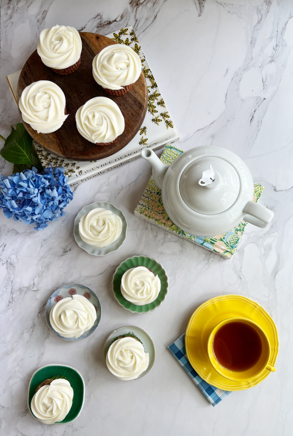 Flatlay of cupcakes a tea pot honeybee books and a yellow cup and saucer