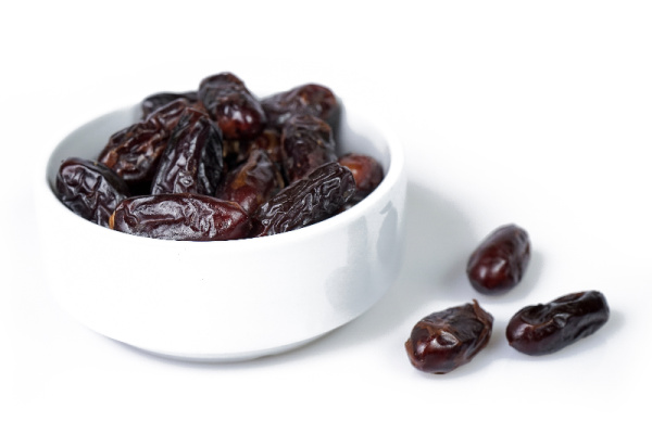 medjool dates in a white bowl with 3 sitting on the side. 