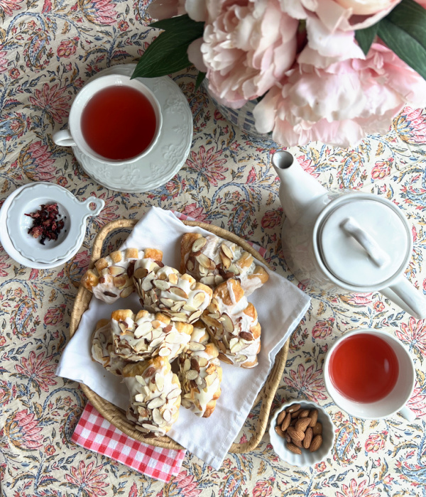 bear claw pastries on a white platter with pink peonies, two cups of tea and a white teapot.