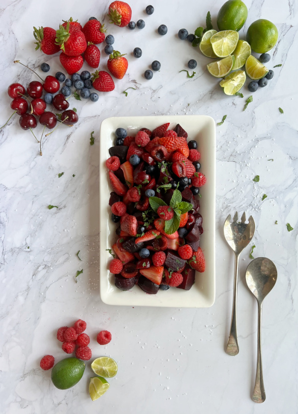 Roasted Beet and summer berry salad on a white platter with a pair of silver salad utensils.
