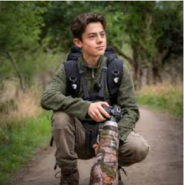 Shelby Grant, image of a young man with a camera kneeling on the ground.