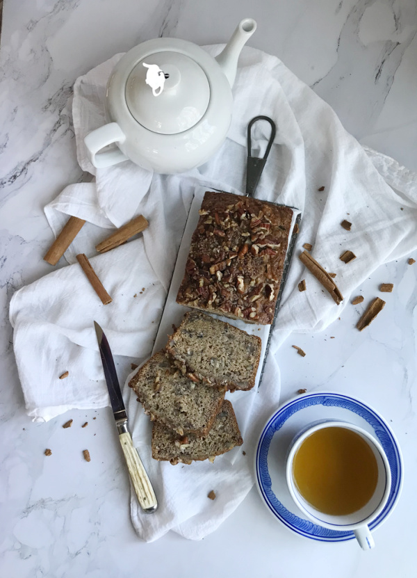 Banana bread with a white tea pot and a cup of tea in a blue and white cup.