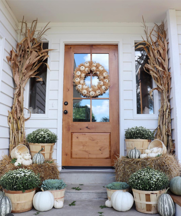 Fall front porch with pale green pumpkins, mums and hay.