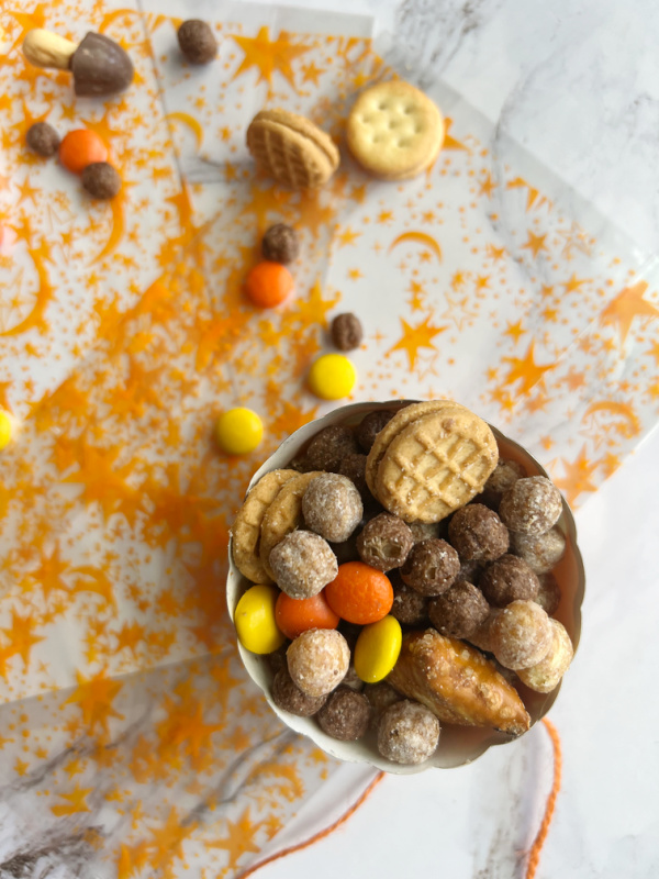 Peanut Butter Fall Snack mix in a pumpkin and scattered with orange twine and orange and white paper cups.