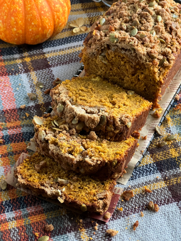 Pumpkin Spice Bread with Pepita Streusel Topping, an orange pumpkin on plain tablecloth.