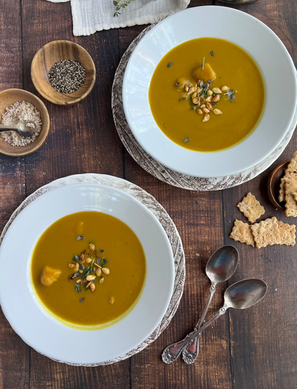 butternut squash soup and spoons with crackers in two white bowls.