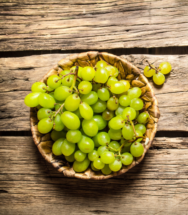 green grapes in a bowl sitting on a wood plank.