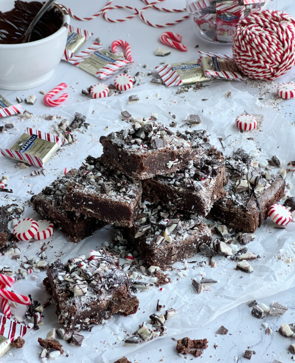 A bowl of melted chocolate a pile of peppermint brownies and a ball of red and white twine.