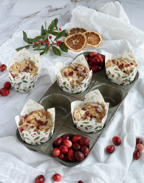 Cranberry Orange Muffins in a muffin tin with scattered cranberries.