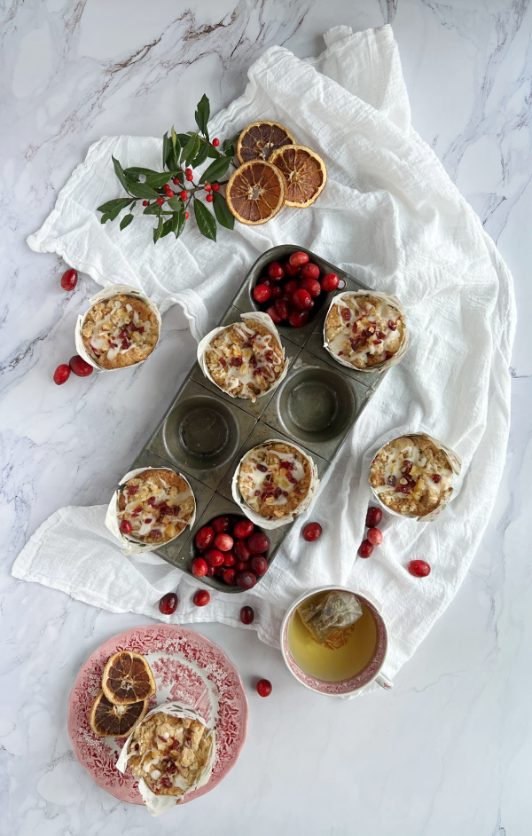 Cranberry orange muffins in a pan and a cup of tea in a ed and white transfer ware cup.