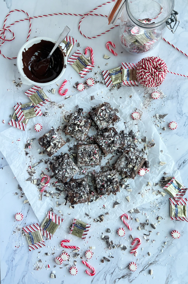 peppermint bark brownie flatlay with a bowl of chocolate, brownies, scattered candy canes and chocolates.