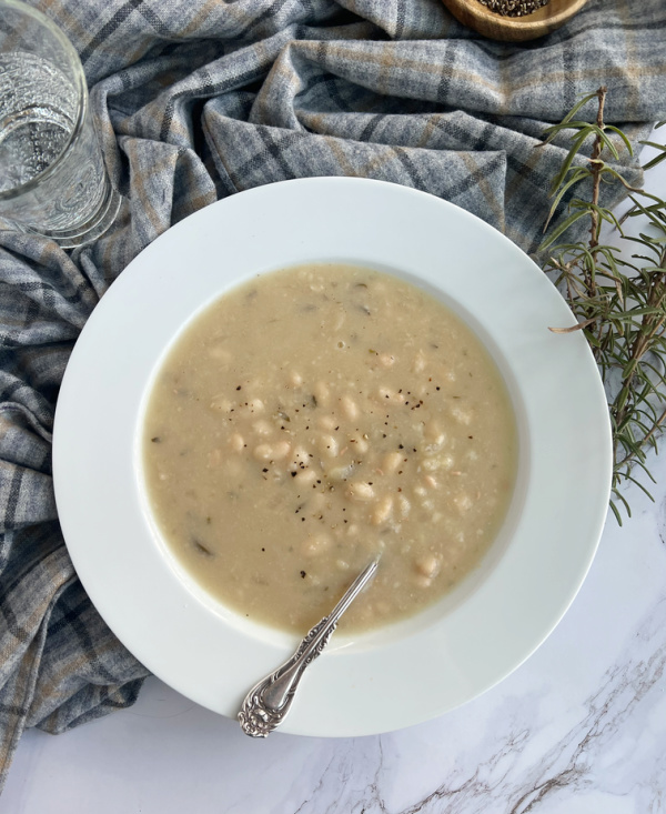 Barefoot Contessa Rosemary white bean soup in a white bowl. with a spoon sitting on a gray plaid throw.