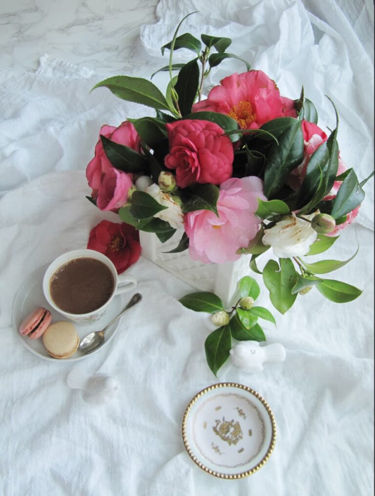 camellia blossoms in a vase with a cup of hot chocolate.