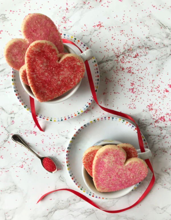 two cups filled with red and pink heart shaped sugar cookies and sprinkles.