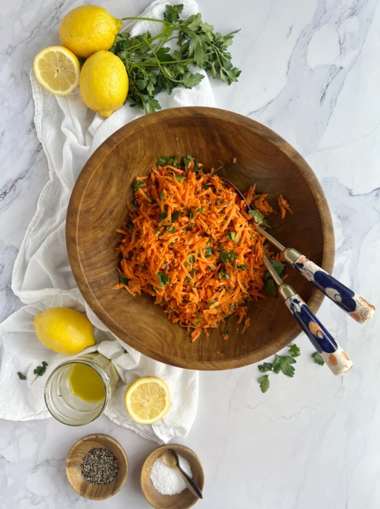 French carrot salad salade de carottes râpées — classic French bistro grated carrot salad with lemon dressing and flat-leaf parsley in a wood bowl. 