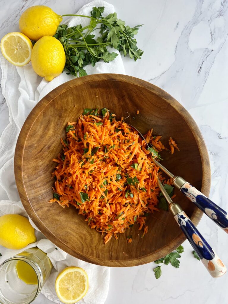 French carrot salad salade de carottes râpées — classic French bistro grated carrot salad with lemon dressing and flat-leaf parsley in a wood bowl with scattered lemons.