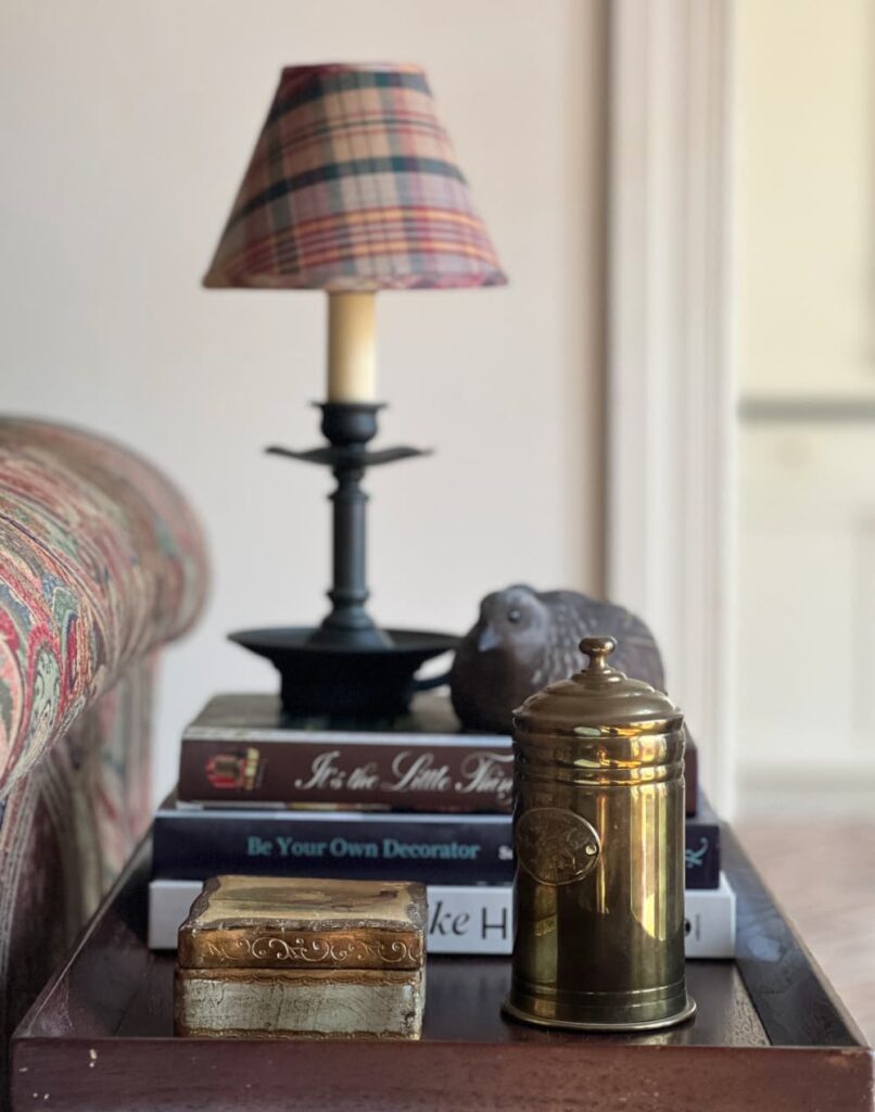 Maximalist home decor pile of books, vintage brass canister, carved bird, Florentine box.