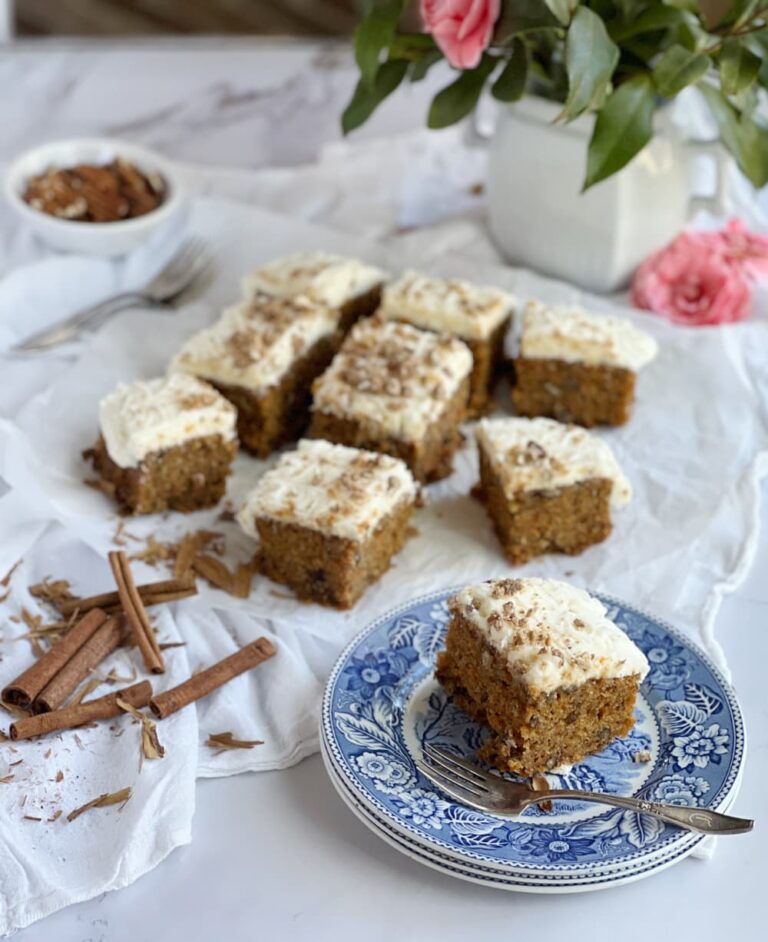 Sliced carrot cake with a stack of blue and white plates and an owl of pecans.