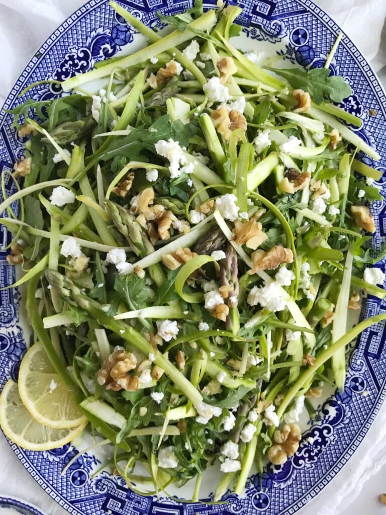 haved asparagus salad with feta cheese and lemon slices on a blue and white platter.