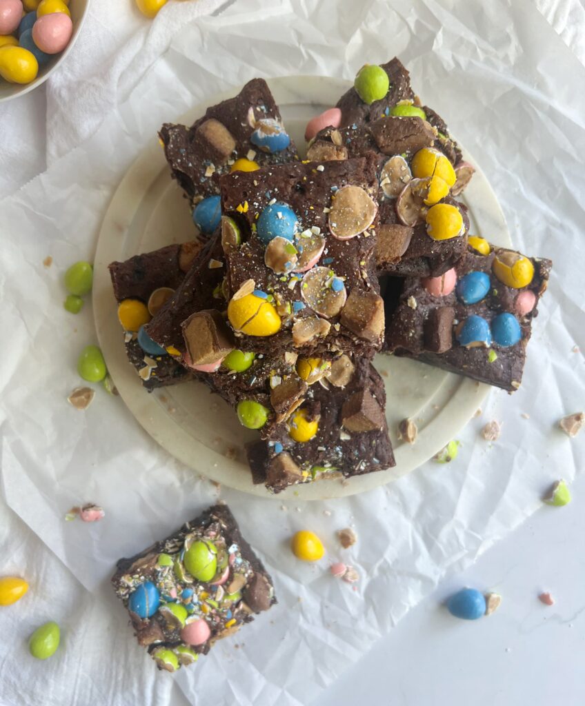 Reeses Easter brownies cut and on a piece of round marble with a bowl of Reeses pieces.