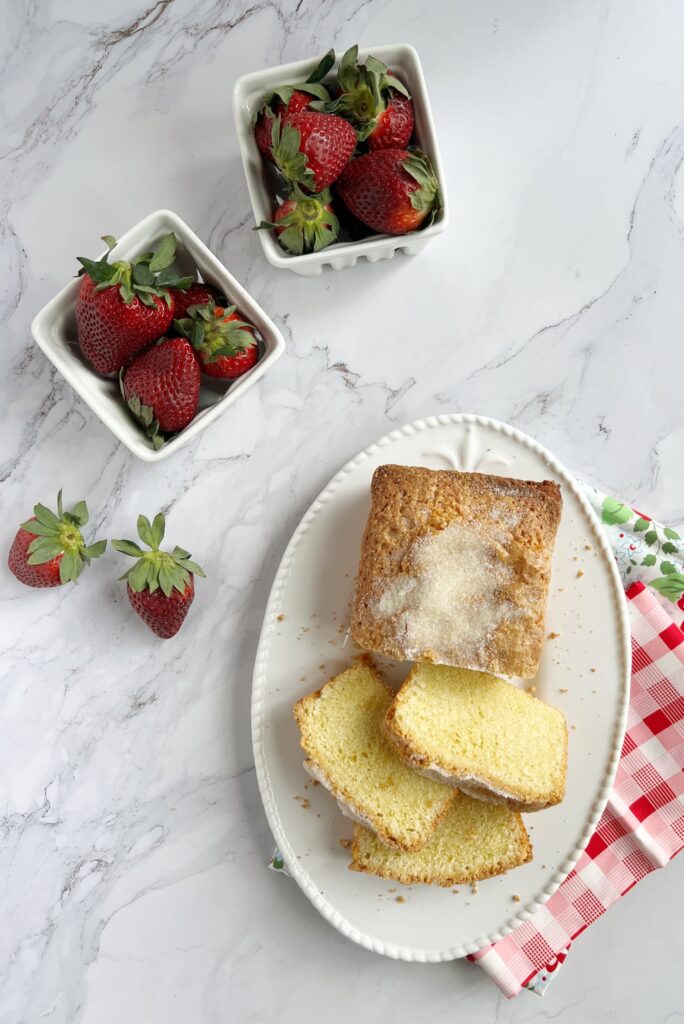 Slice of brown butter pound cake on a white platter with two white ceramic baskets filled with strawberries.