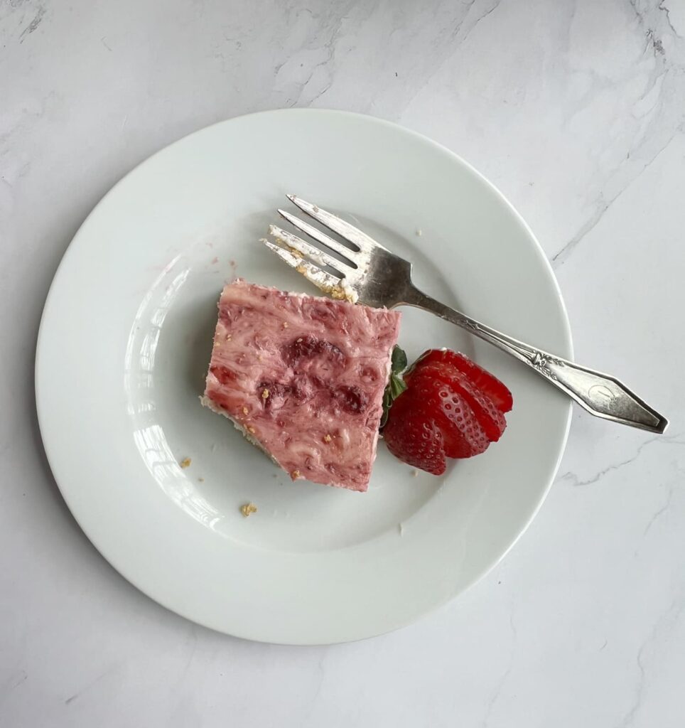 cheesecake bar on a white plate with a fork and a strawberry