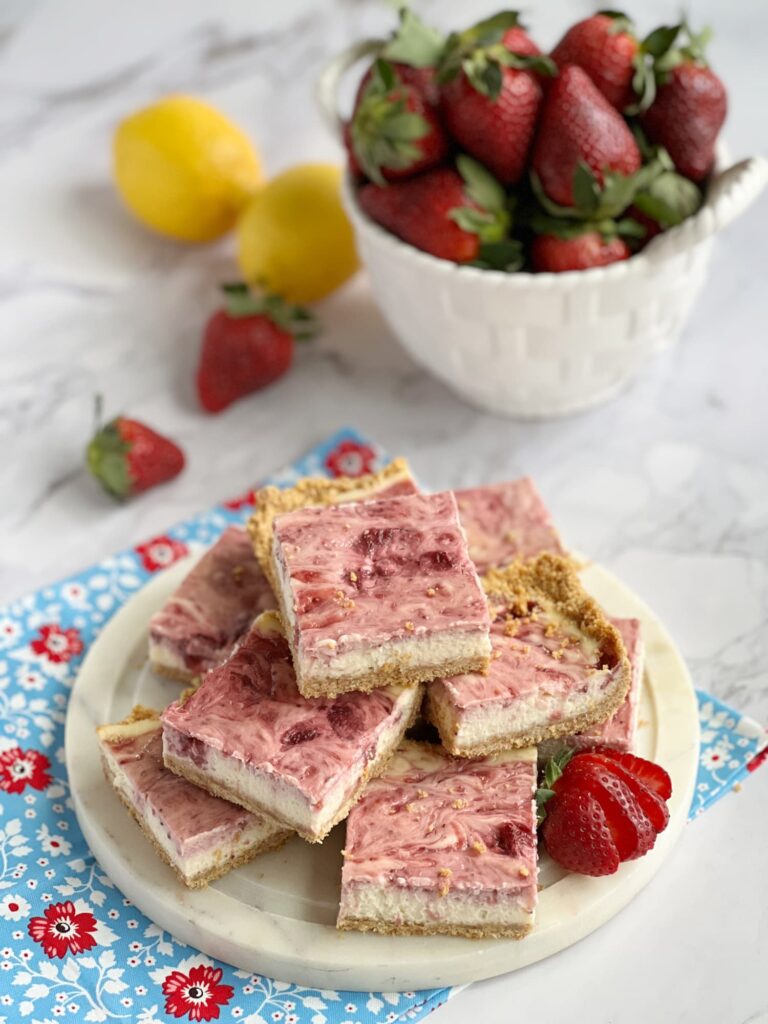 summer-strawberries in a white bowl with strawberry swirl cheesecake bars on a platter