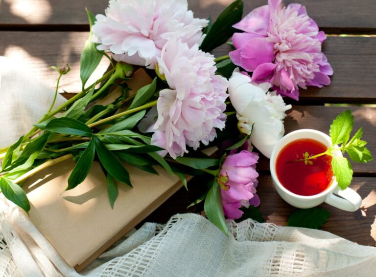 7 books to read this spring — a book and a cup of tea on a deck with spring peonies