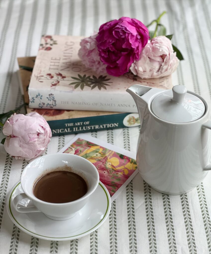 What I’m reading — a stack of well-loved books on a table with a cup of drinking chocolate