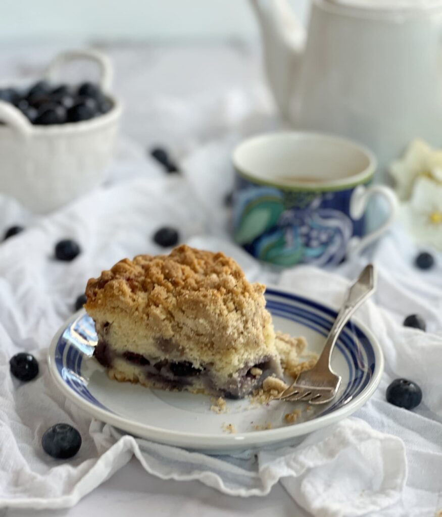 Ina Garten blueberry Crumb Cake on a plate with a cup of tea