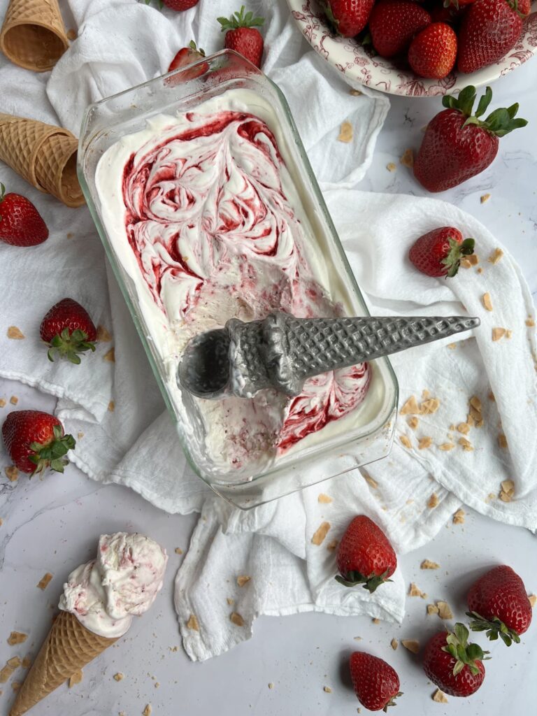 strawberry no-churn swirl ice cream in a clear glass loaf pan with fresh strawberries