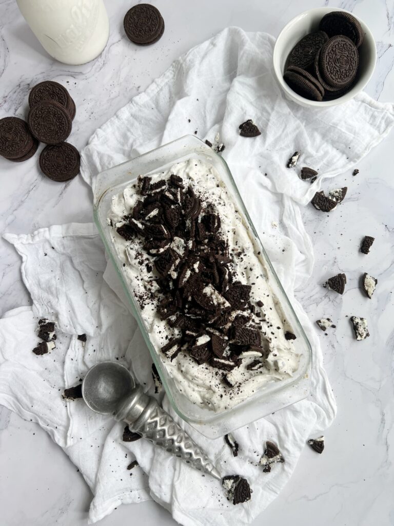 Glass loaf pan of no churn ice cream with a glass bottle of milk and a bowl of Oreo cookies