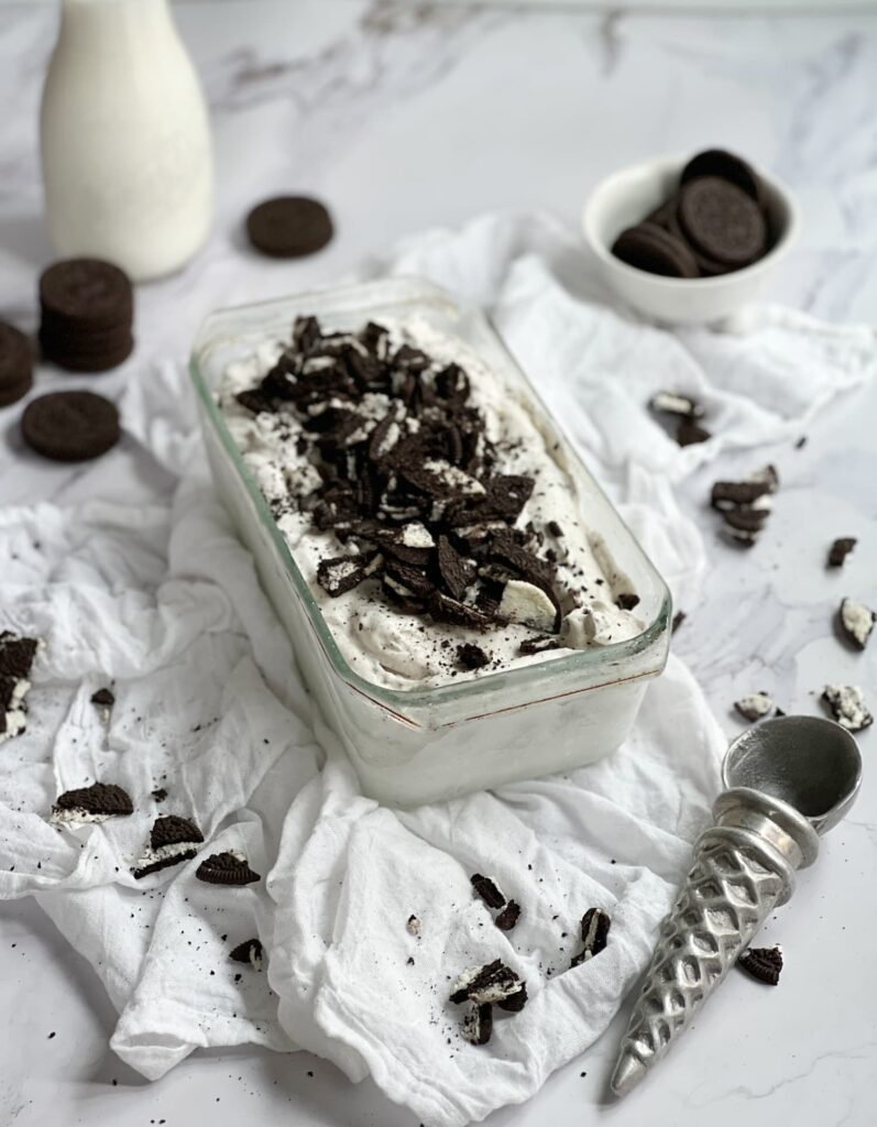 Glass loaf pan of no churn ice cream with a glass bottle of milk and an ice cream cone shaped ice cream scoop
