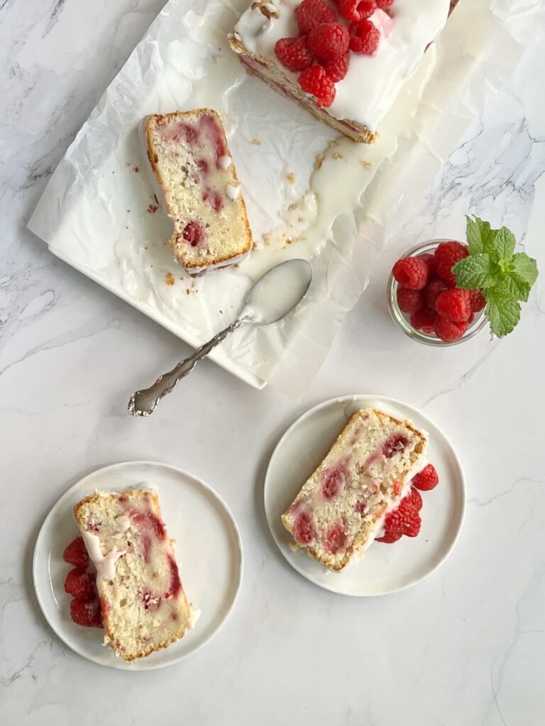 A slice of raspberry lemon loaf cake showing moist crumb and fresh raspberries