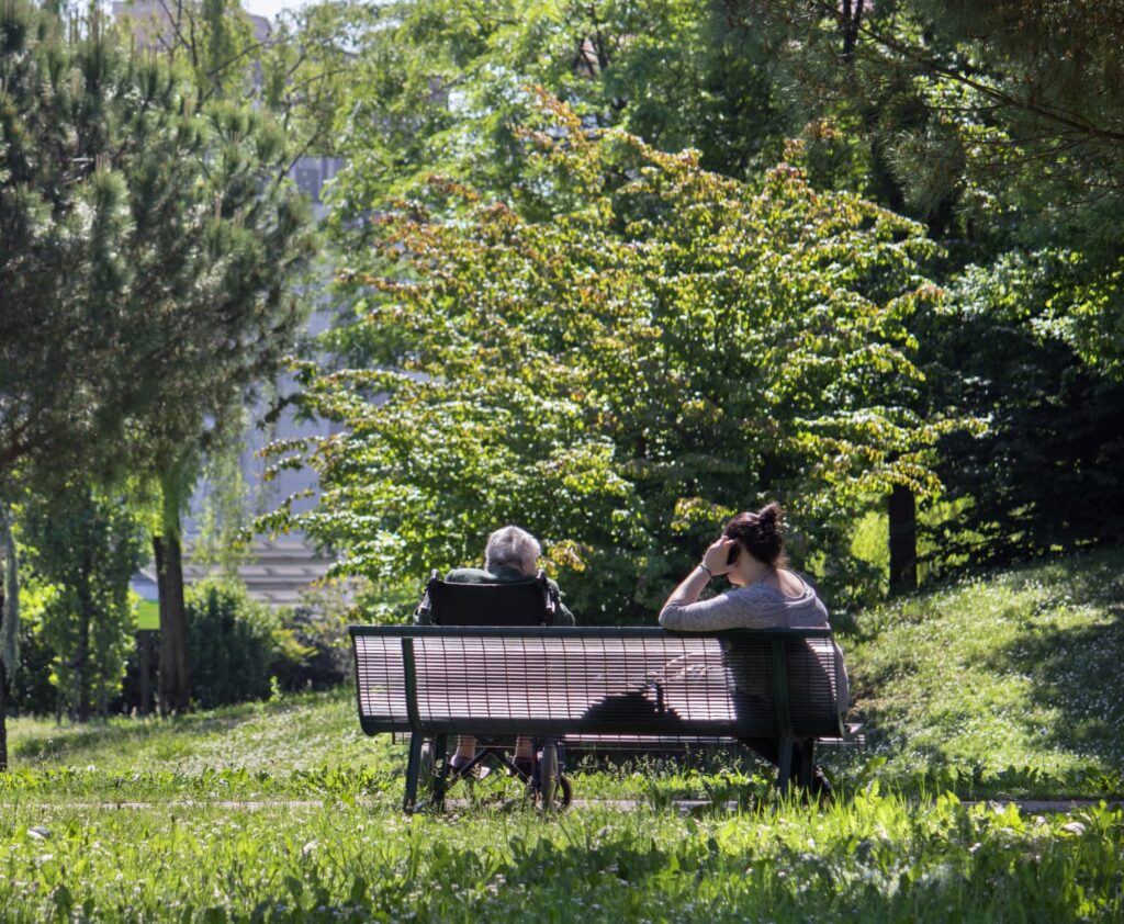 Dear Caretaker, a woman in a wheel chair sitting next to a woman on a park bench