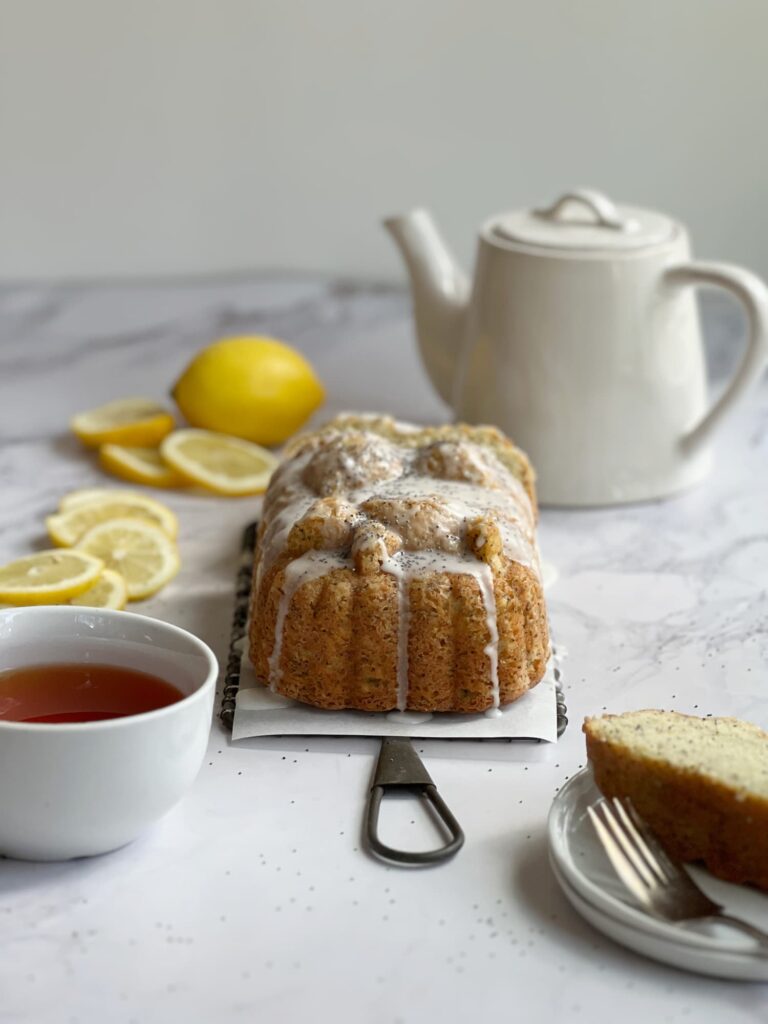 lemon poppyseed loaf cake sliced on a plate with tea in a teapot