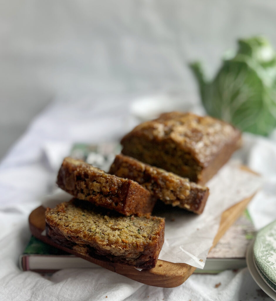 sliced quick bread on a wood cutting board with a green cabbage teapot in the background