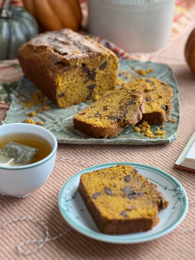 chocolate chip pumpkin bread sliced on a green and white plate with a cup of tea