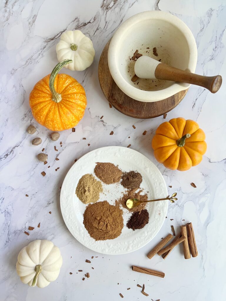 homemade pumpkin pie spice, 6 spices on a white plate with orange and white pumpkins