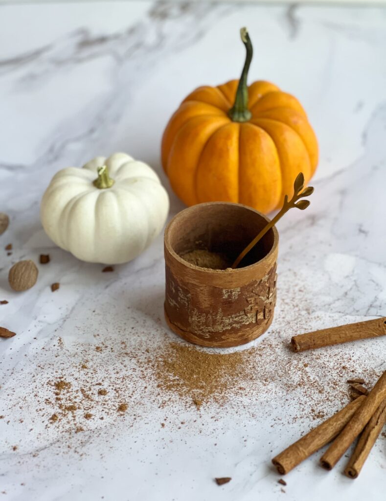 homemade pumpkin spice mix in a wood container with an orange and white pumpkin and cinnamon sticks