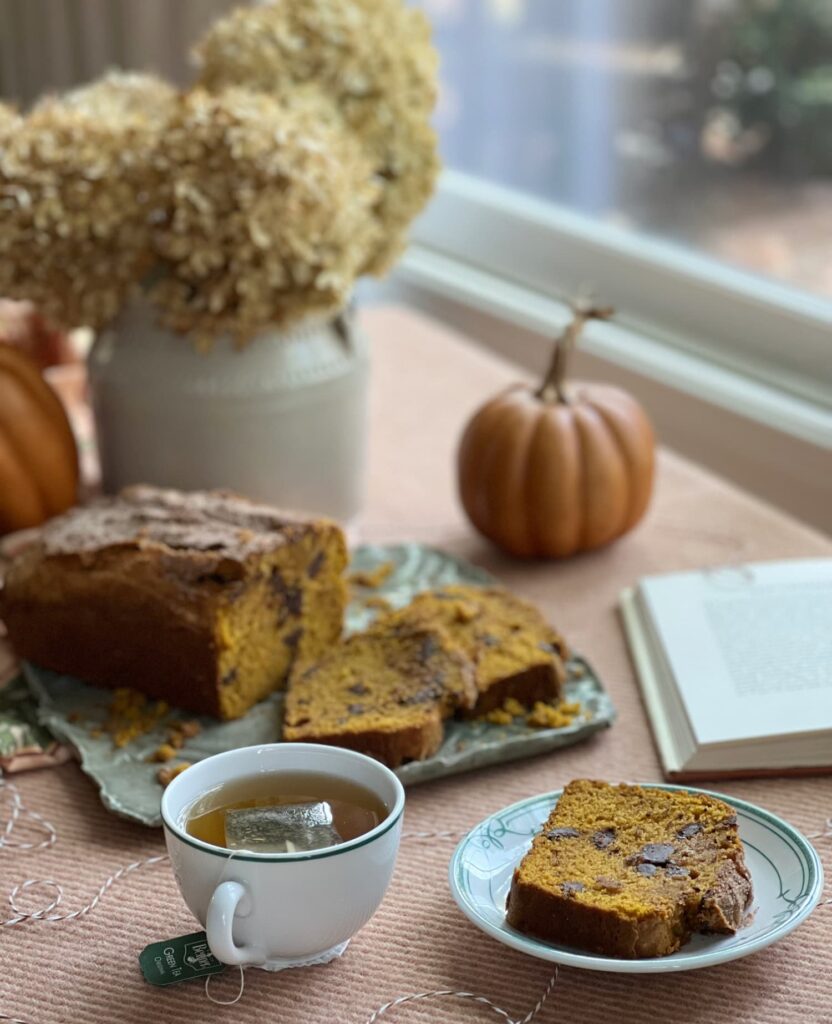 pumpkin chocolate chunk bread on a plate with a cup of tea and a vase of dried hydrangeas